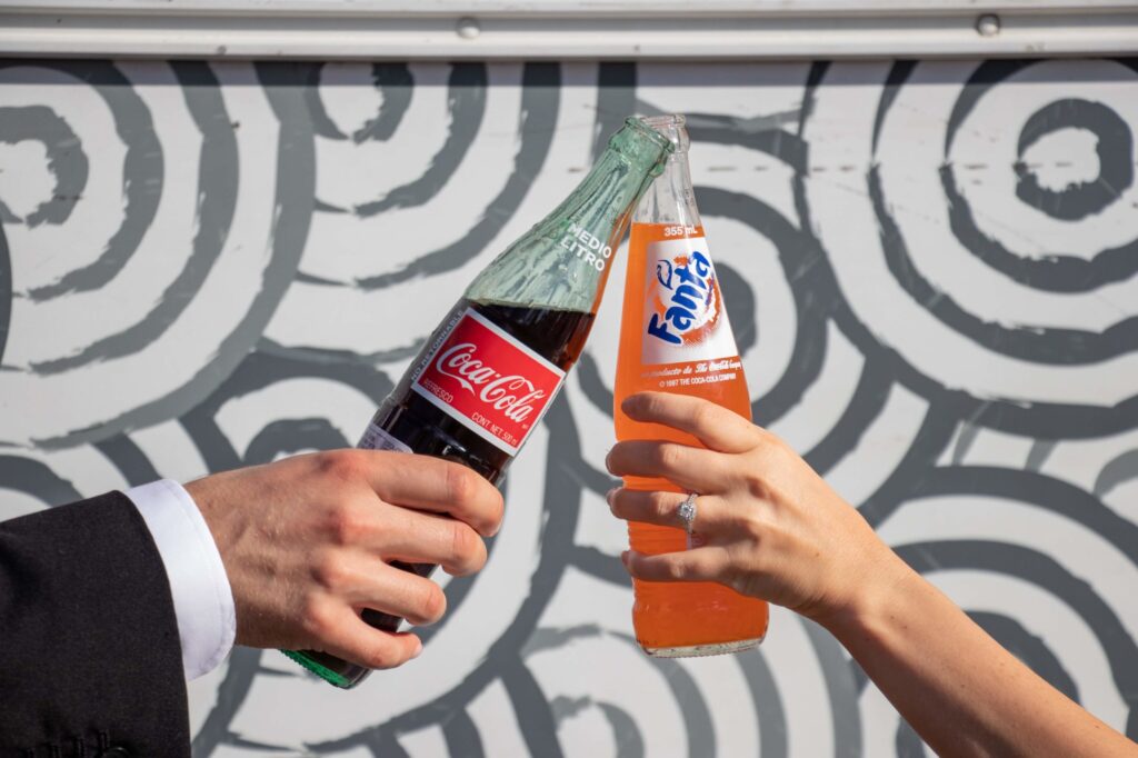 A newlywed couple clinking bottles of soda together, enjoying their wedding catering in Phoenix, AZ