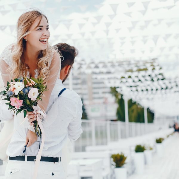 Elegant blonde in a white dress. Couple standing in a park. Bride with bouquet of flowers. Man in a white shirt