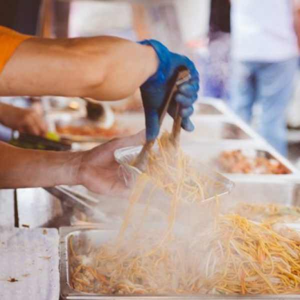 person in orange shirt putting spaghetti in aluminum container